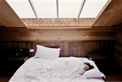 Woman sleeps on white bed in room with glass ceiling