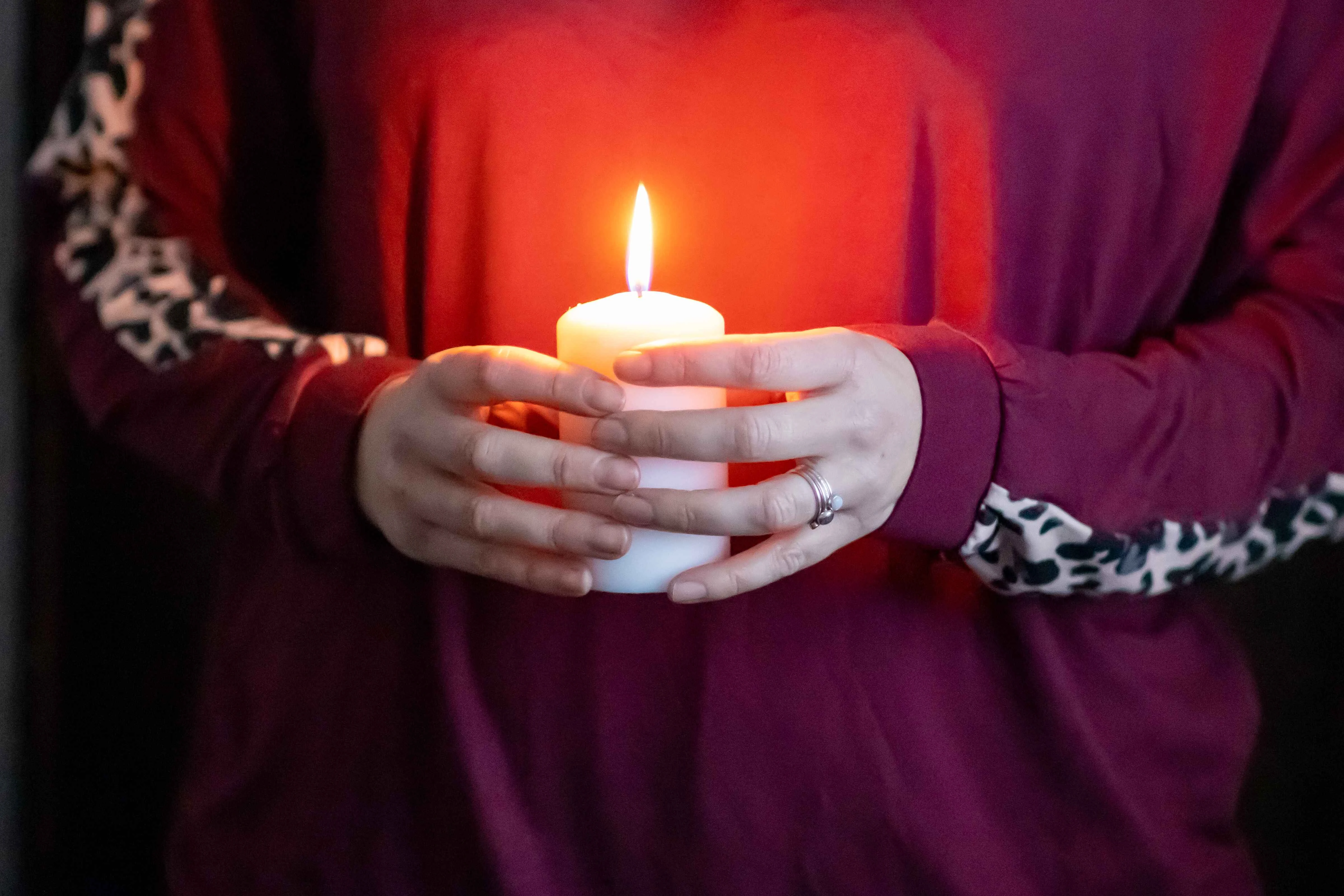 A close up of someone holding a candle while wearing deep red loungewear with leopard print detailing