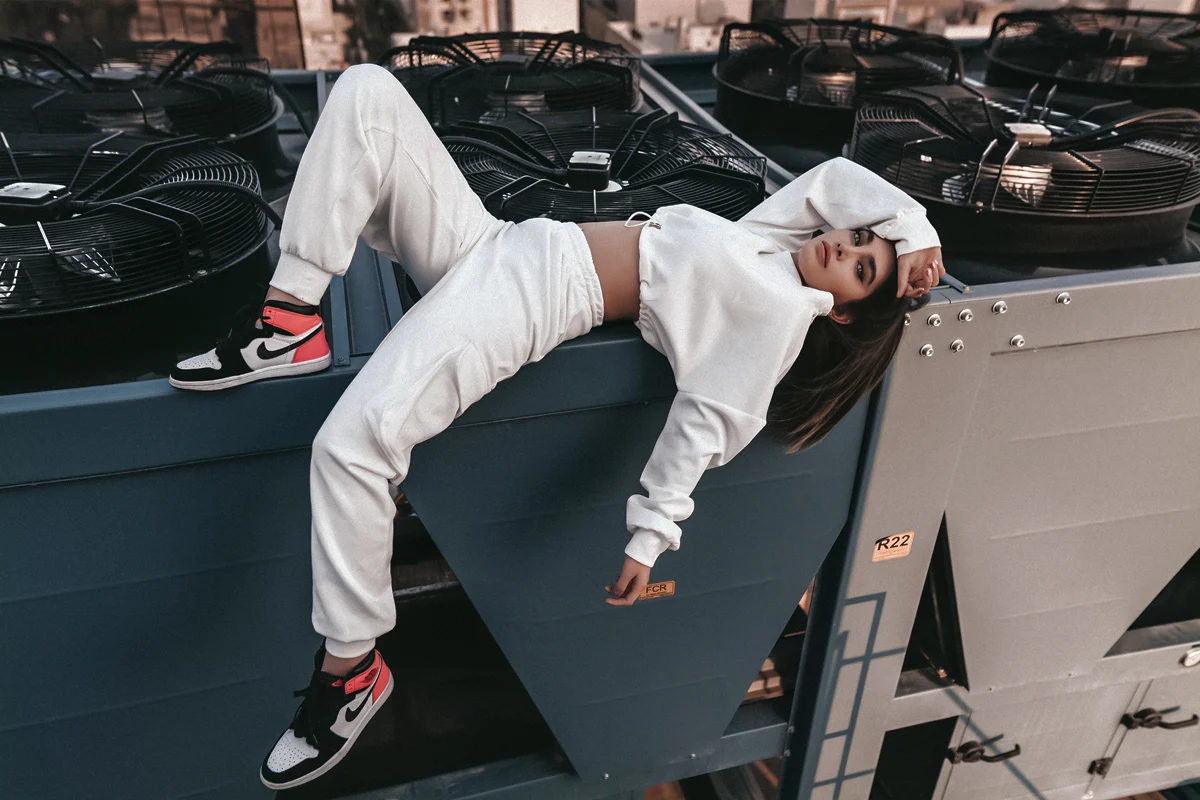 woman in a white sweatsuit is posing on a roof