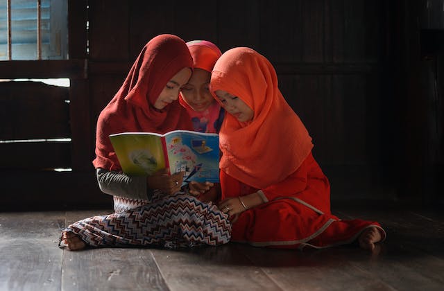 three young girls sitting on the floor reading a book together