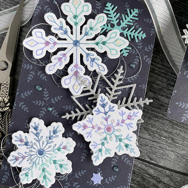 Ombre stamped snowflake tags created with: Scrapbook.com dainty snowflakes stamp and die set, peppermint patterned paper, solar white cardstock, pops of color lavender luster royal blue teal twinkle snowflake, snowflakes die, glitter metals paper; Tim Holtz distress oxide salvaged patina shaded lilac, faded jeans