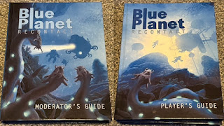 Photo of the two Print-On-Demand test copies of the Blue Planet Recontact core books. They both show stunning underwater images in the oceans of Poseidon with humans swimming above and menacing eel-like creatures below.