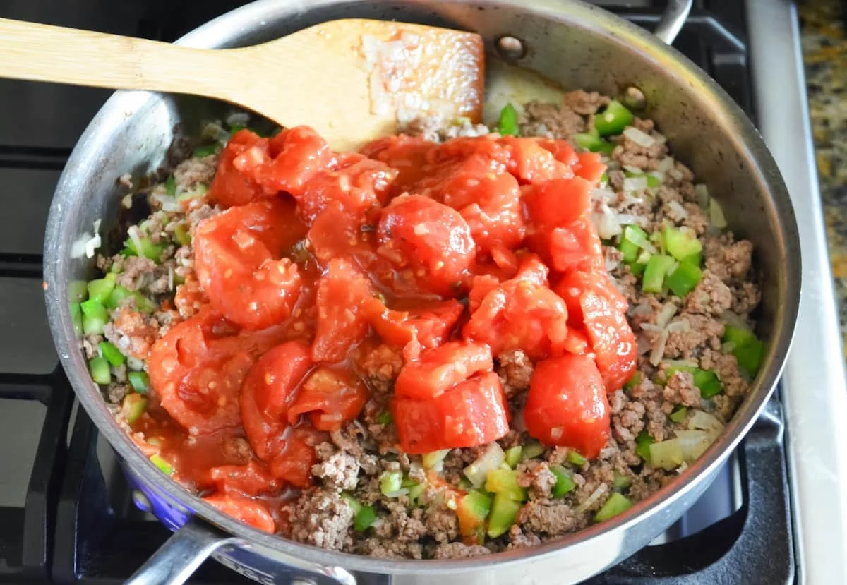 A stainless steel skillet with browned ground beef, onion, garlic, chopped bell pepper, and diced tomatoes