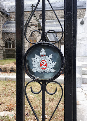 Element of a metal fence showing a round glass covered disc featuring a gold and red military cap badge