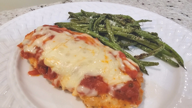 Healthy chicken Parmesan on a plate with roasted green beans.