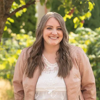 smiling young woman standing in front of green foliage