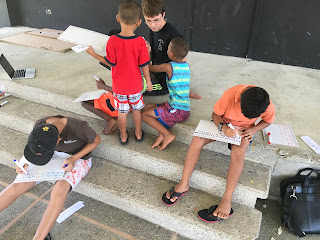 Orphans on the concrete stairs writing the alphabet on portable white boards.