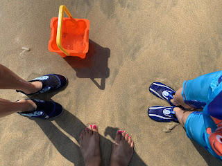 Three pairs of feet standing in a circle on sandy beach 