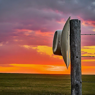 A classic cowboy hat hanging on a fence post, bathed in the warm glow of a Texas sunset, creating a serene and nostalgic atmosphere.