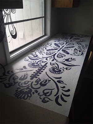 A white plywood counter with a bold folk art floral design in deep indigo-purple, lit with clear white light from the window centered over the counter.