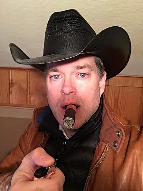 Handsome blue-eyed Cowboy wearing an orange leather jacket and hat smoking cigar
