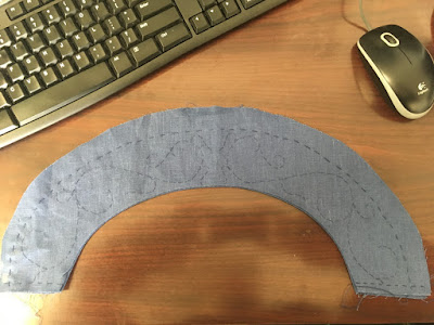 A half-circle band of blue linen with a panel marked out in blue thread and the main vine pattern marked in basted stitches.