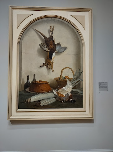 Photo of a trompe l'oeuil (fool the eye) painting, called "The Pate." The painting is done to look as if it's real object in a wall niche, including a pate encrusted in bread,  a dead rabbit and dead game fowl hanging down, a couple of bottles of wine, a couple of squash (I think), and another deal game fowl on the same surface as the wine and the paté.