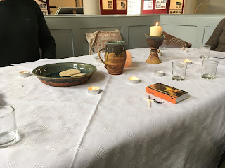 Worship table pretty much as it was set out before us.  White table cloth.  A candle in a "chalice" (a ceramic goblet), some tea light candles and boxes of matches around the edge.