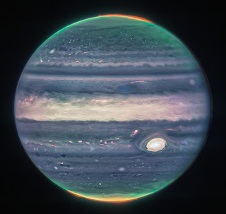 This 07/27/22 image of Jupiter taken by the Near-Infrared Camera on the new James Webb Space Telescope is artificially colored to emphasize stunning details of the planet: auroral emission from ionized hydrogen at both the north and south poles (red); high-altitude hazes (green) that swirl around the poles; and light reflected from the deeper main cloud (blue). The Great Red Spot, the equatorial region and compact cloud regions appear white or reddish-white; regions with little cloud cover appear as dark ribbons north of the equatorial region.