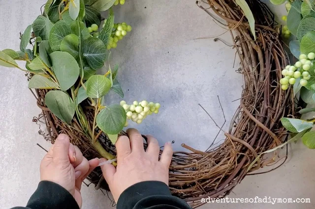 Tightening the zip tie to hold the greenery wreath frame to the grapevine wreath form.