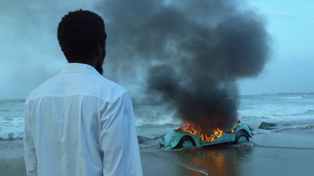 a man watches a car burn on a beach