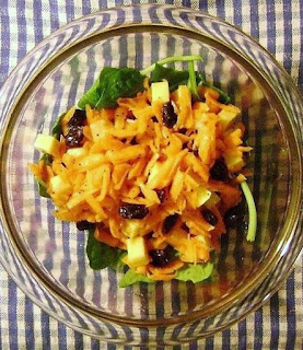 Main-dish vegan carrot salad with poppyseed dressing on a bed of fresh spinach.