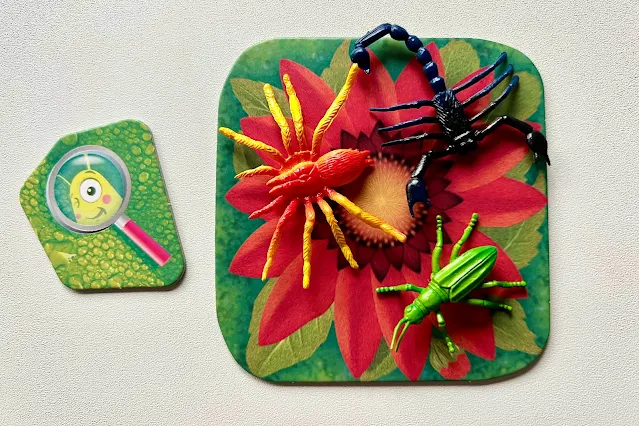 A flower card, a magnifying glass token and 3 plastic creatures