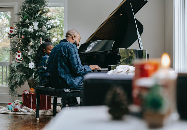 Hombre y niña en pijama tocando el piano junto a un árbol de navidad