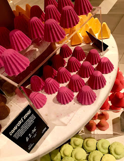 A collection of ridged tear drop shaped reddish pink shower bombs on a white shelf with comfort zone in white font on a square black card on a bright background