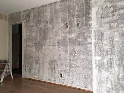 A large, lightly skim-coated wall, looking a lot like a poorly rendered computer grpahic between the occasional trowel lines and the brown paint showing through the white drywall mud.