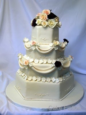 A four tiered hexagonal shape wedding cake adorned with a selection of ivory