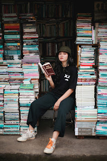 Chica sostiene un libro y está rodeada de pilas de libros.