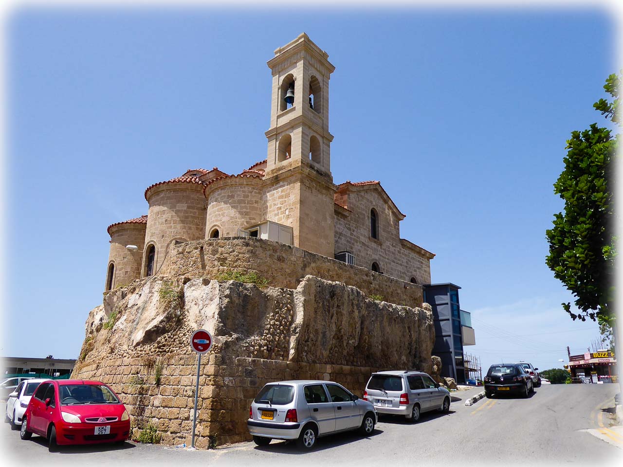 Kościół Panagia Theoskepasti znajdujący się na kamiennym wzgórzu, otoczony drogą z zaparkowanymi samochodami.