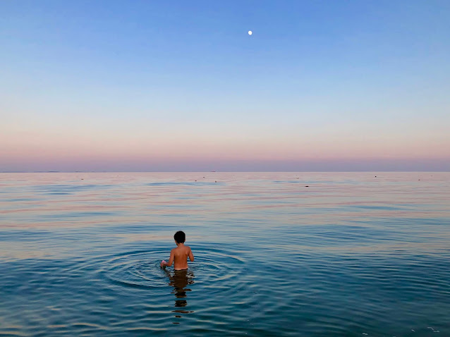 Boy in calm water on the bay with colorful sky after sunset