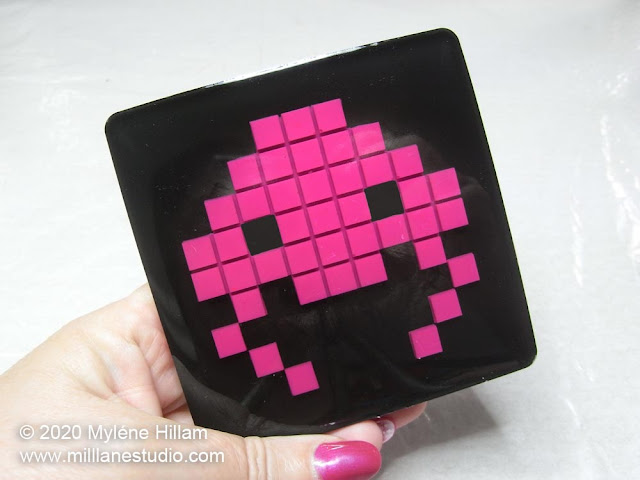 Hand holding the finished bright pink and black jellyfish space invader resin coaster