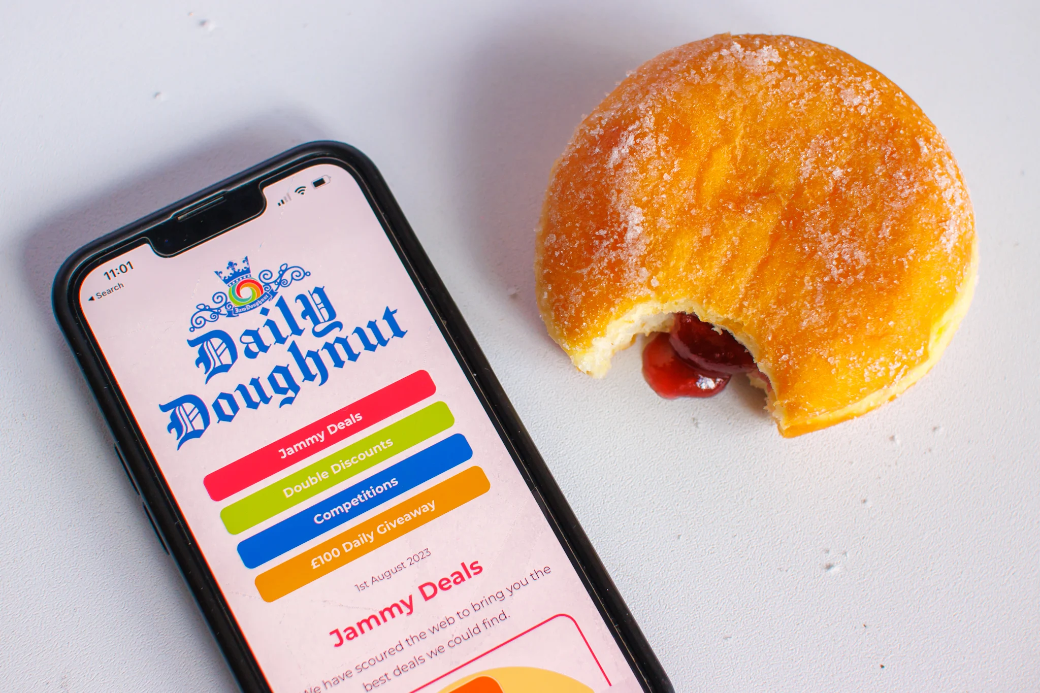 A phone with the JamDoughnut app open next to a jam doughnut