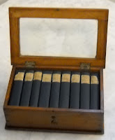 A photograph of nine miniature books in an open wooden case with a glass top.