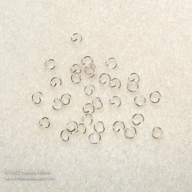 Bunch of opened silver jump rings on a cream beading mat