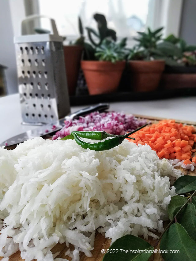Grated white daikon radish or mooli with green chilies and a grater, knife and onions in the background.