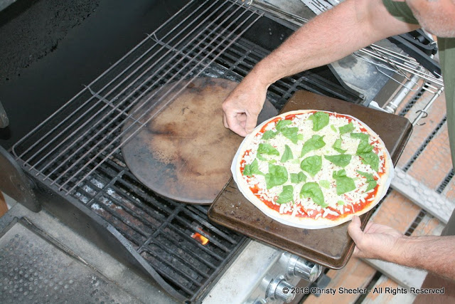 A pizza is being transferred to a preheated pizza stone on the grill.