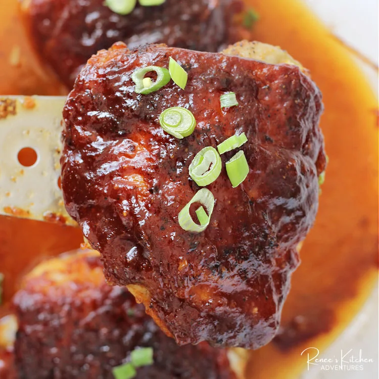 One perfect bbq chicken thigh on a spatula being lifted from the pan covered in gooey bbq sauce