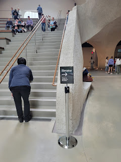 Central stairs, with a free-standing sign pointing off to the side for the elevator