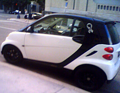 This a picture of a white Smart Car with a Human Society Ribbon on visible behind the windows.