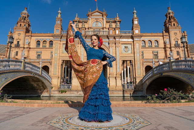 Mujer con traje de flamenca y mantón de manila frente al edificio principal de la plaza de España de Sevilla.