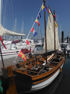 small wooden boat with white sail up and dressed over all with signal flags