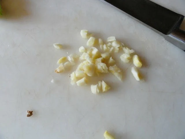 Chopped garlic on a white cutting board with a knife laying on it's side.