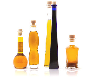 4 frascos compridos com óleos de cor amarela e uma garrafa comprida azul, todas fechadas com rolha.