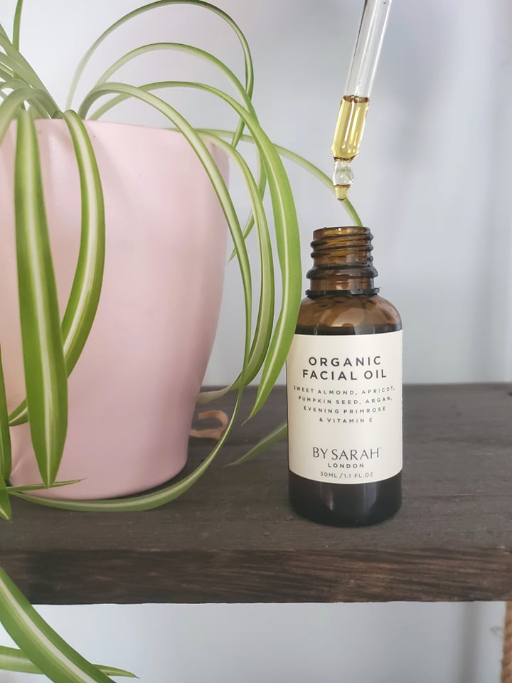 Organic Facial Oil from By Sarah London on a hanging shelf next to a spider plant