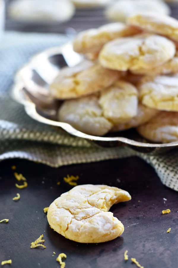 Lemon cake mix cookies on a silver tray with a single cookie that has a bite out of it setting in front of the tray