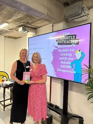 Blonde haired woman in black dress next to silver haired woman in pink dress, both holding the ADHD book