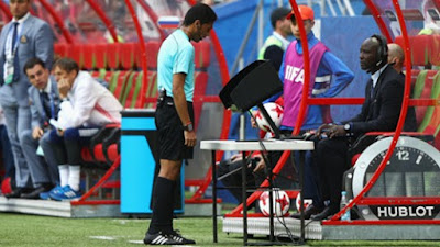 Árbitro de futebol em frente ao monitor do VAR revisando uma jogada.