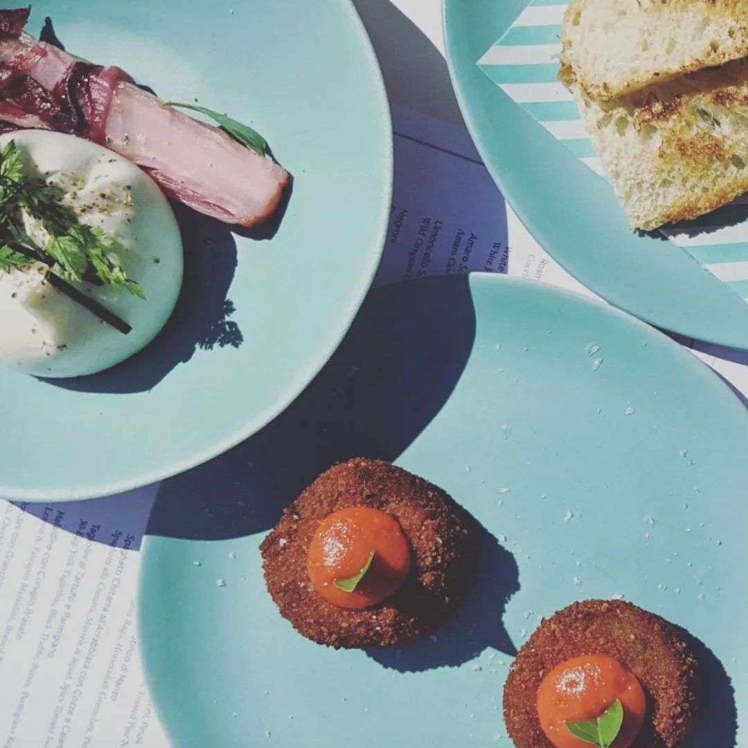 blue plates laid on a table with burrata and croquettes on them at Lina Stores, one of the most authentic italian restaurants in london