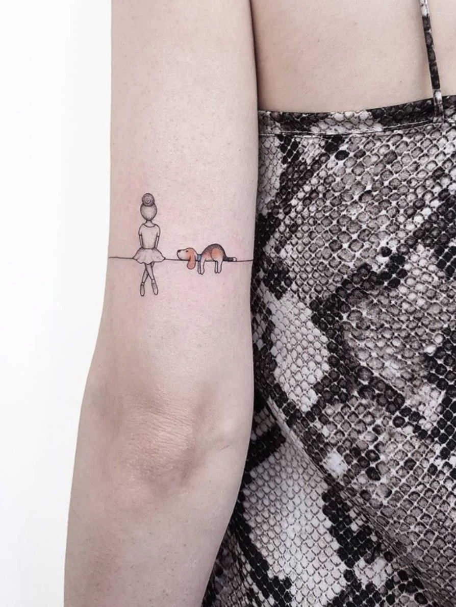 Foto del brazo de una chica que luce el tatuaje de un perro con una niña en una cuerda sentados