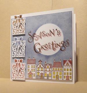 Christmas card, houses with a moon above, Season's Greetings sentiment and 3 presents on the left
